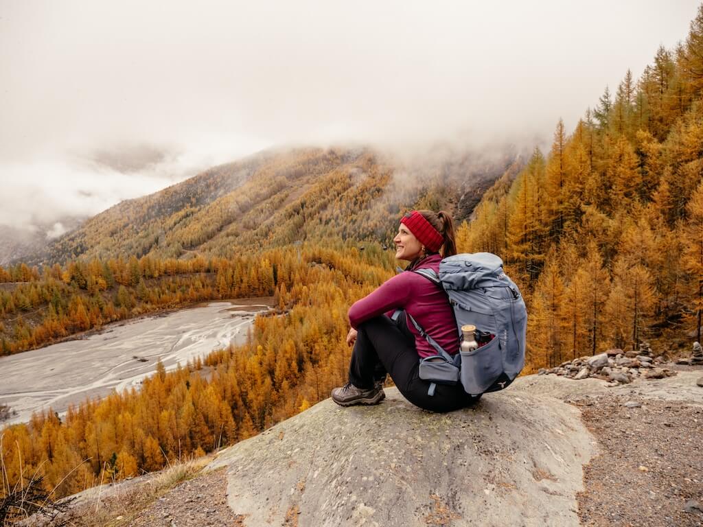 Person sitzt am Gletschersee zwischen Lärchen